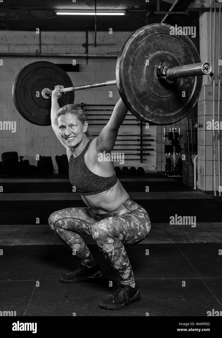 An handsome middle aged female athlete with Sixpack is doing overhead squats with the barbell. Functional fitness and weight lifting workout in a gym. Stock Photo