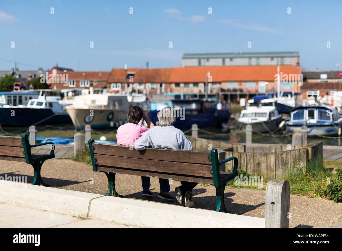 A middle aged couple sitting on a bench admiring the array of different boats moored up in the river Stock Photo