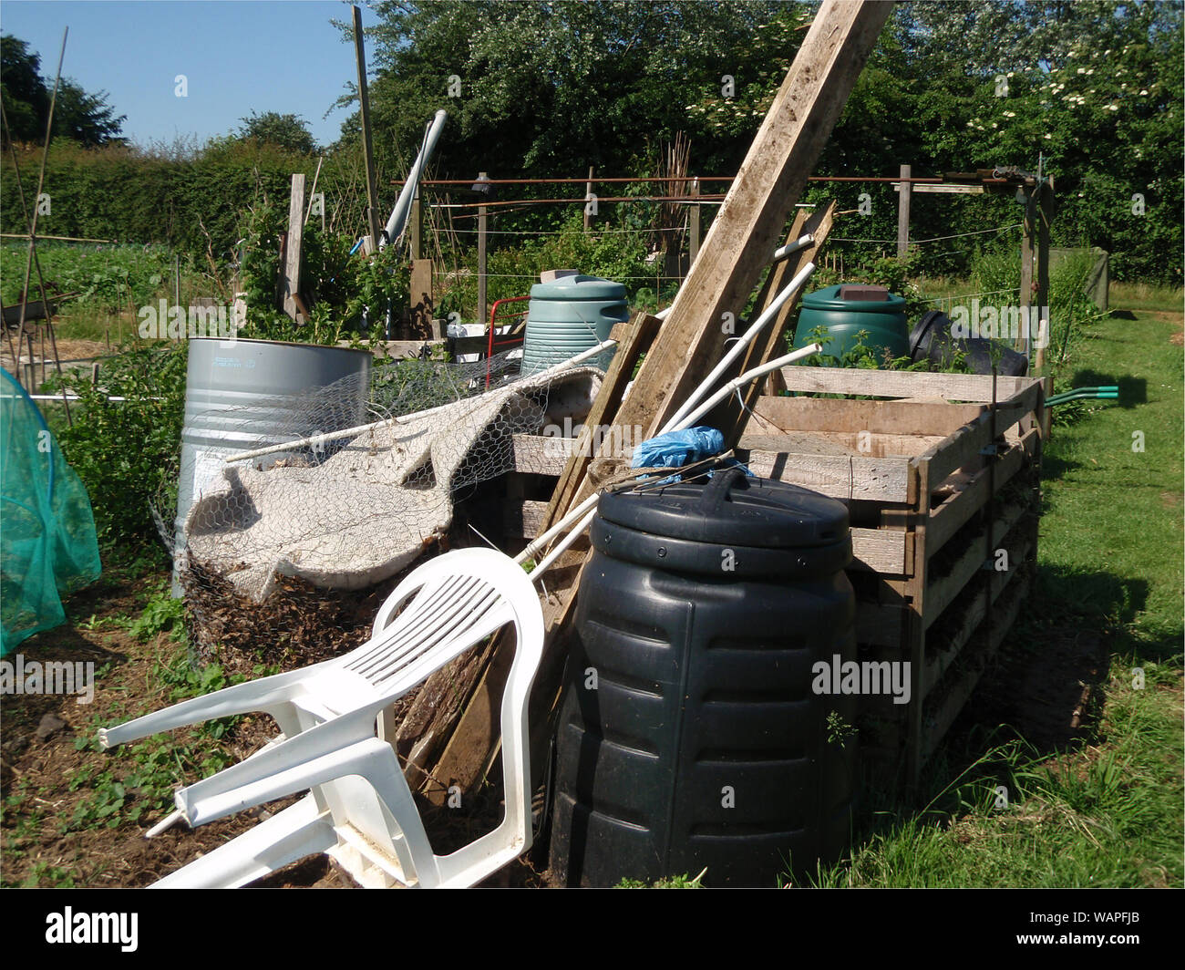 A view looking across an allotment garden with a collection of items of compost bins, sticks, plastic chair, netting, wooden container and fruit frame Stock Photo