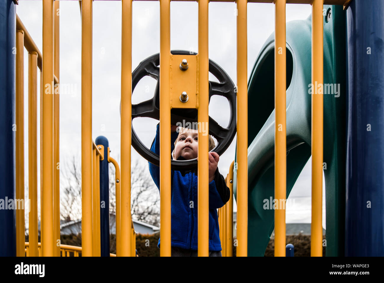 Toddler on playground looking curiously at play steering wheel Stock Photo