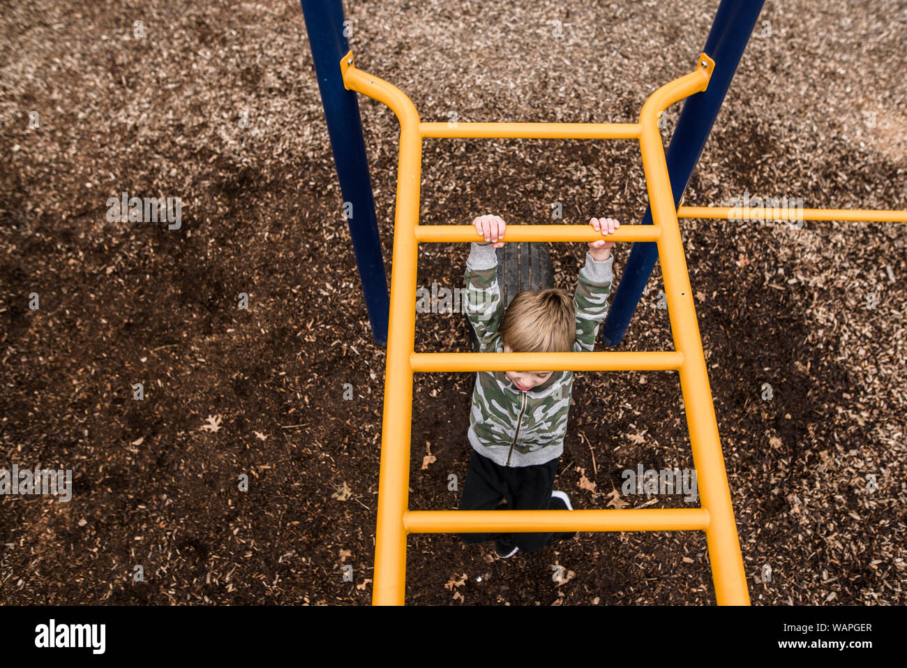 looking down from above at young boy going across monkey bars at park Stock Photo