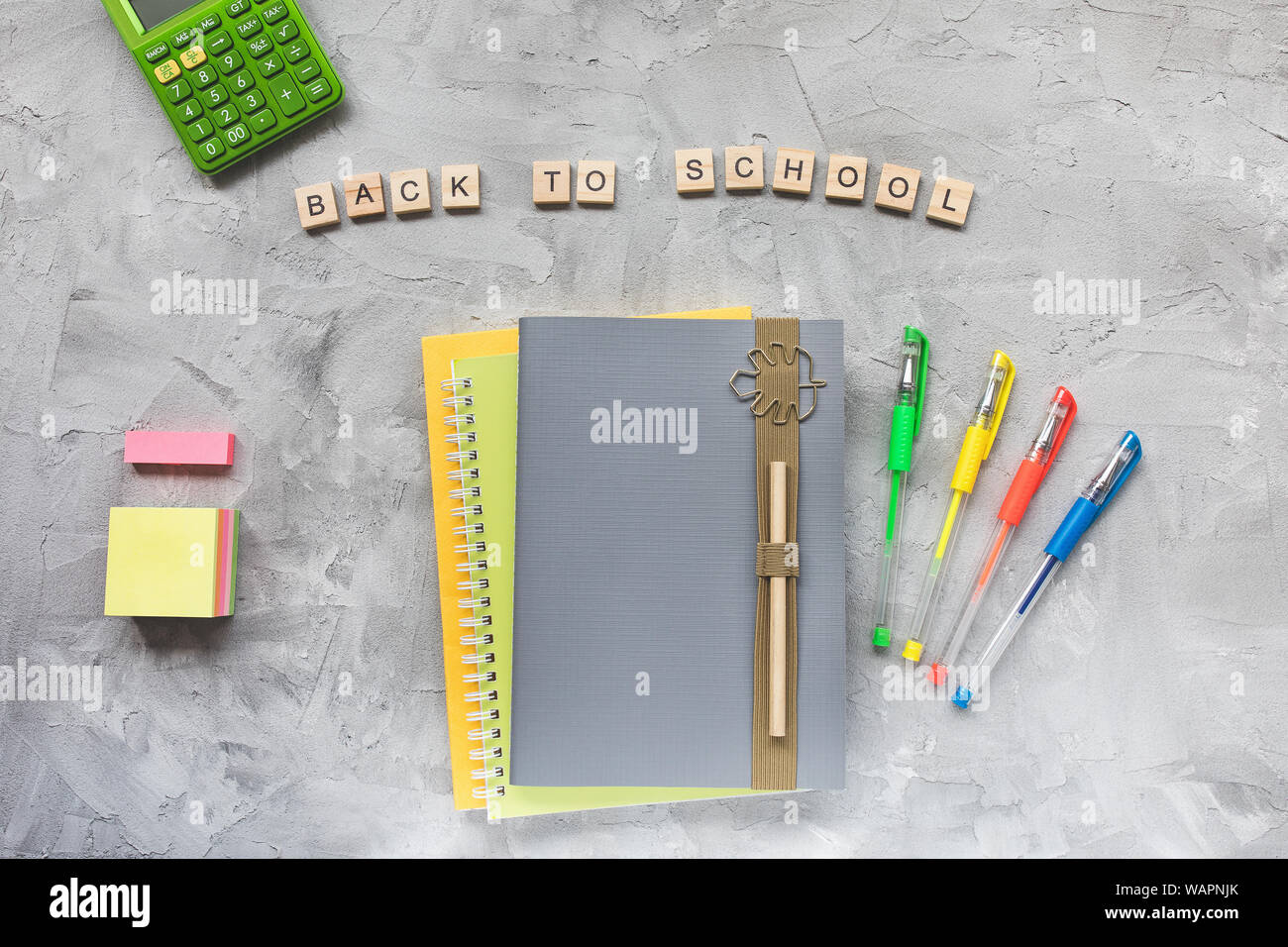 Words BACK TO SCHOOL, notebook, pencil, pens and calculator on a gray background. Education or studying concept, flat lay, top view, social media hero Stock Photo