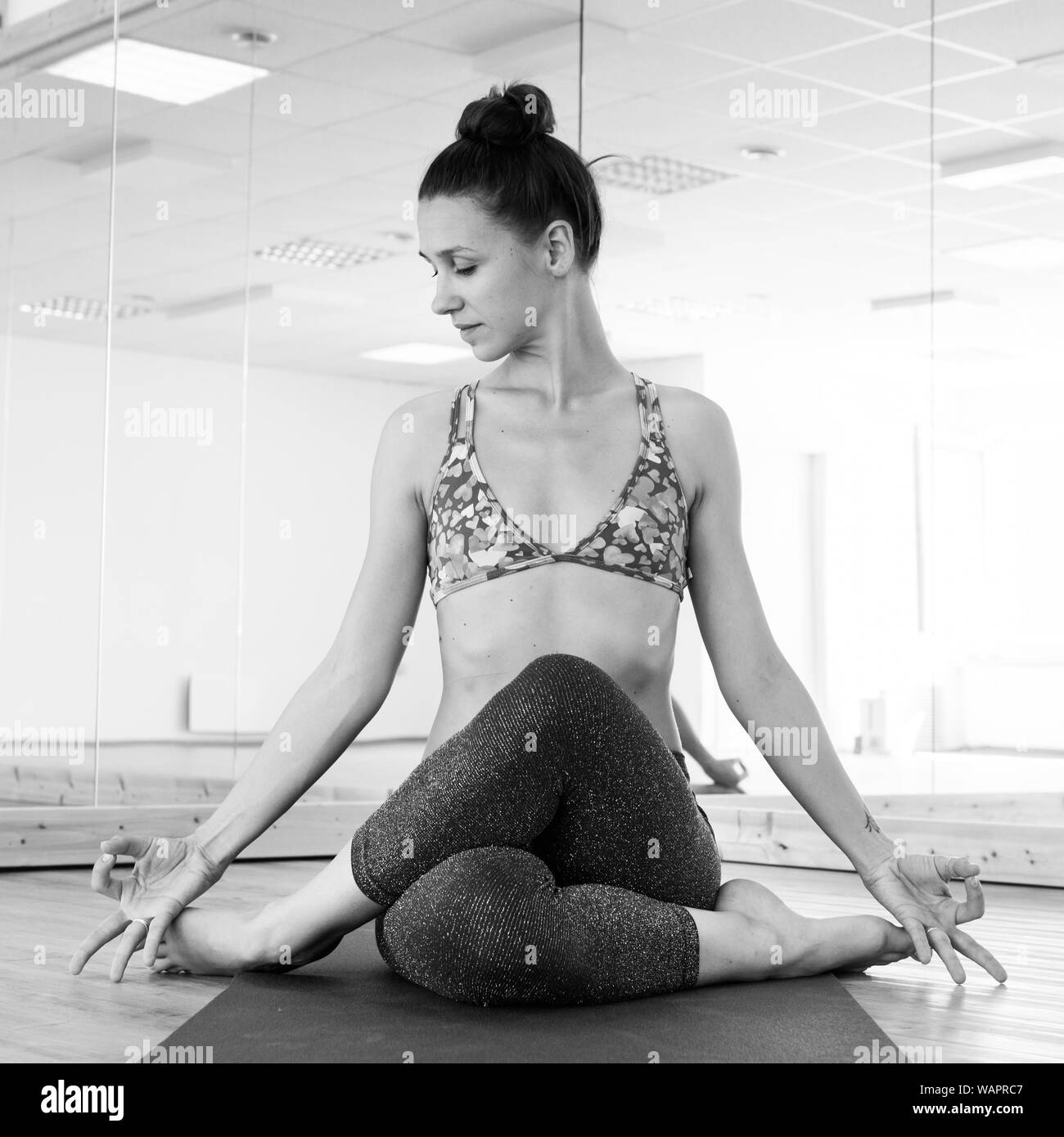 Fit sporty active girl in fashion sportswear doing yoga fitness exercise in yoga studio. Active urban lifestyle. Black and white image. Stock Photo