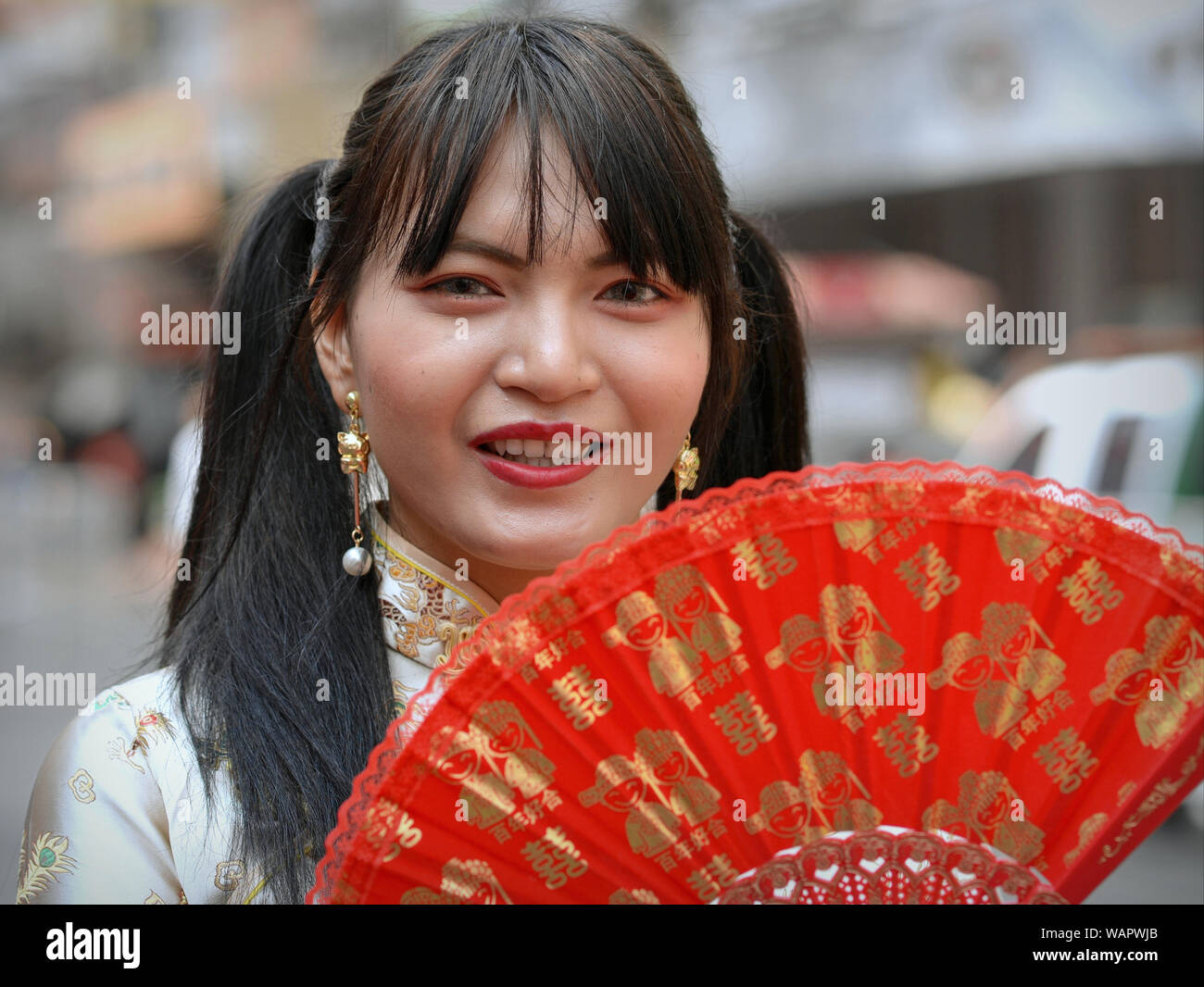 Young Thai woman with long pigtails posesg with a traditional hand-held fan during Chinese New Year. Stock Photo