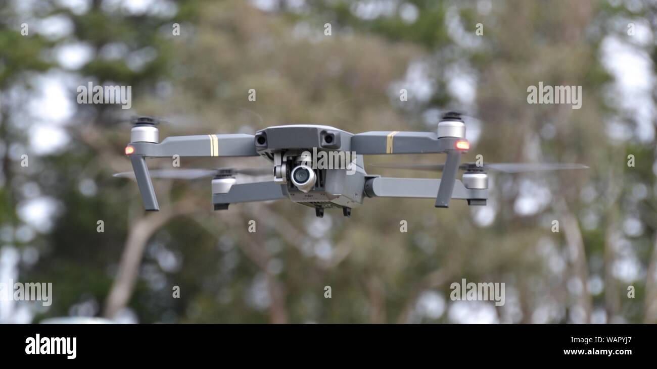 Airborne quadcopter commercial drone hovering in close up with trees in