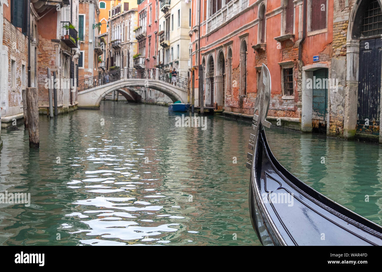 The bow of a gondola, depicting no gondolier, navigating one canal at Venice Stock Photo