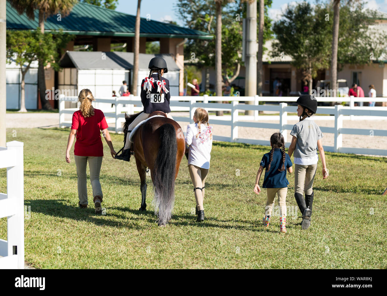 Equestrian kids of different ages and a horse are walking back to the barn after the competition Stock Photo