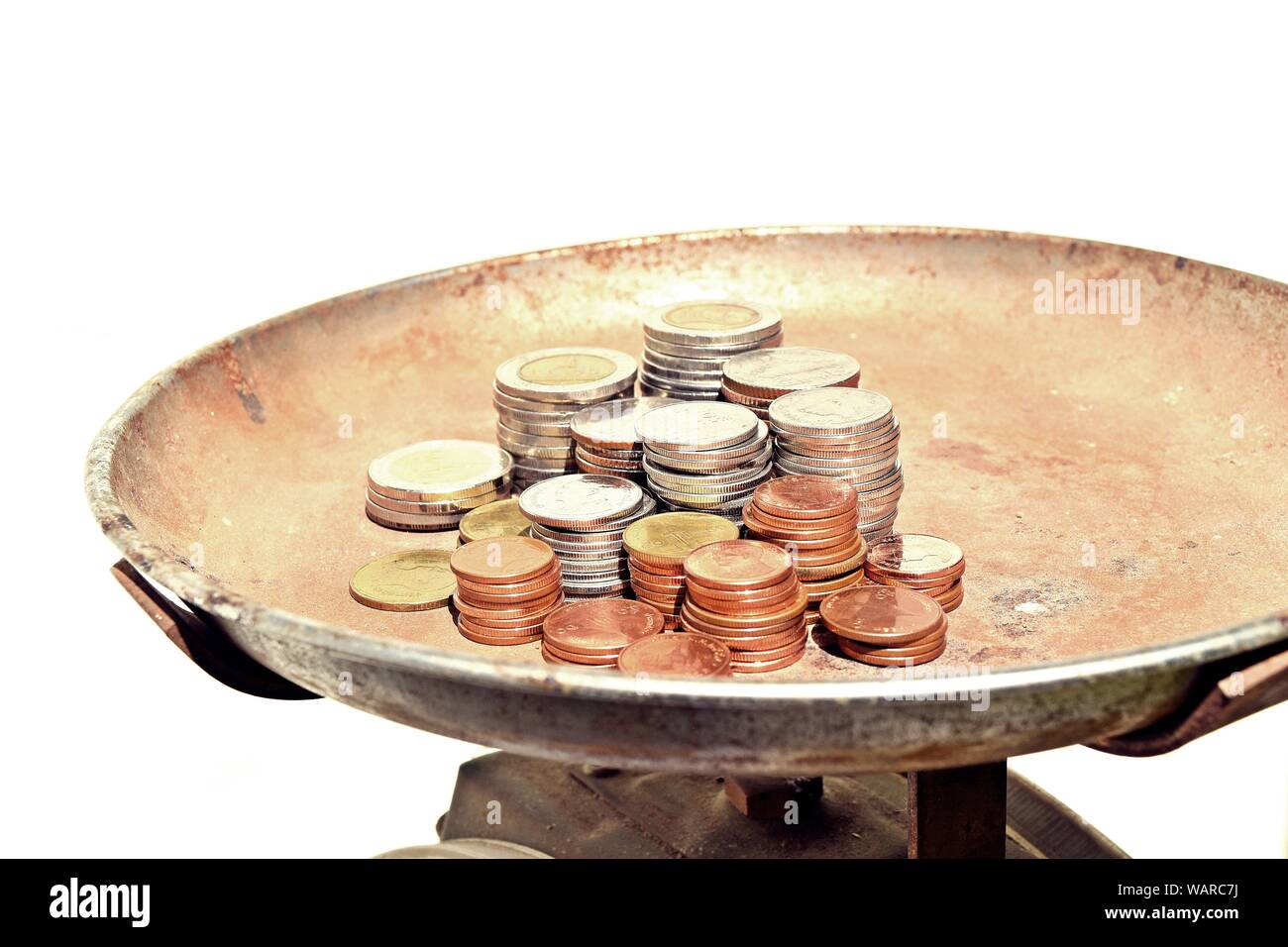 Many stacks of coins in various sizes and valued on vintage kitchen scales on white background, Financial and commit business concept Stock Photo