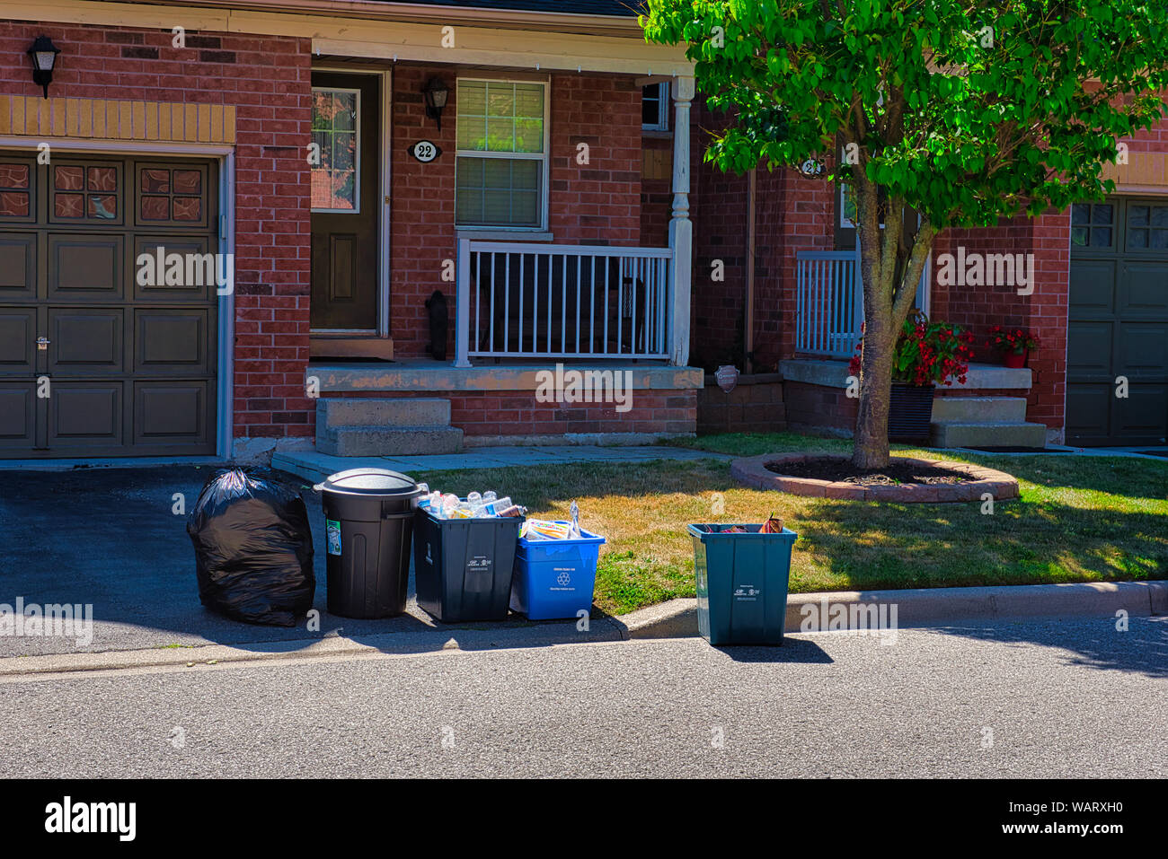 Garbage, recycling and food waste bins are waiting to be picked up in front of a house on garbage day. Stock Photo