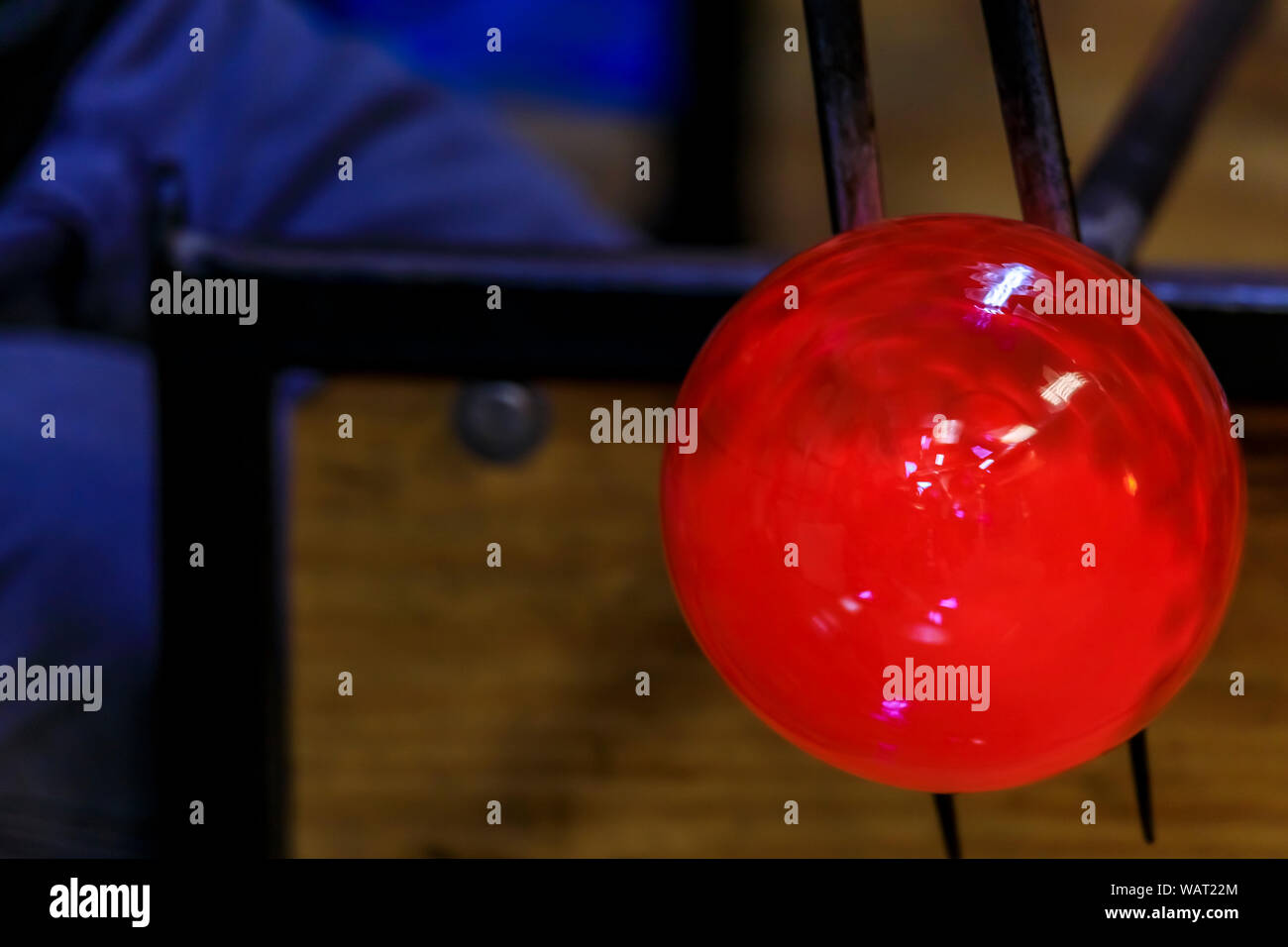 Glass blower shaping a bubble of melted glass on a rod by hand in the