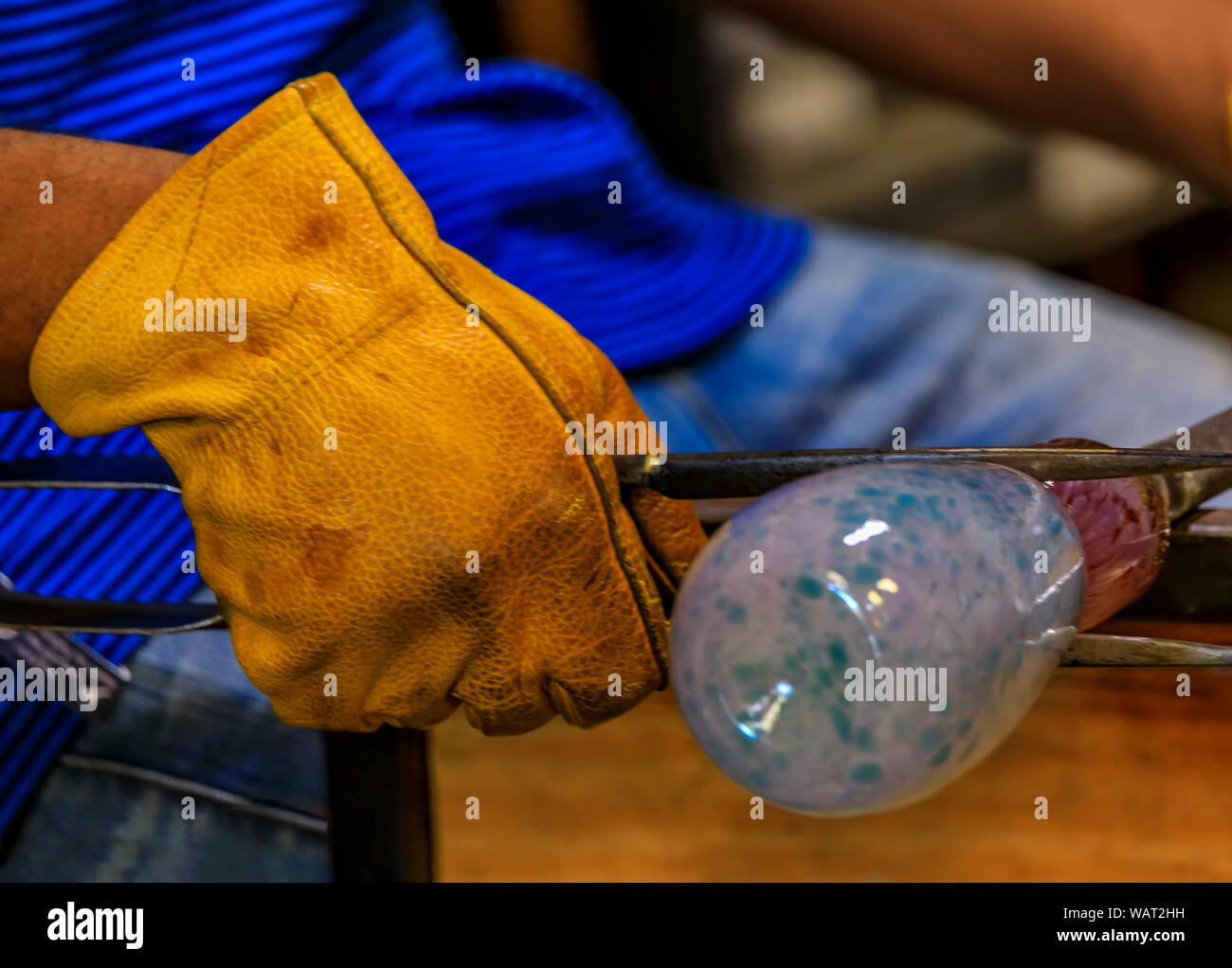 Glass blower shaping a bubble of melted glass on a rod by hand in the