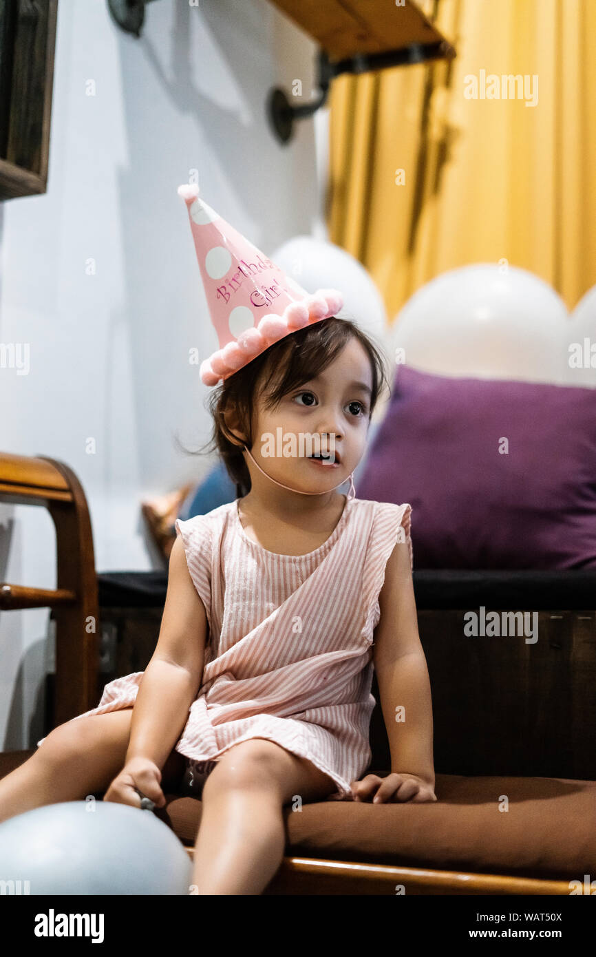 Asian toddler girl is celebrating birthday and wearing a pink hat and holding a baloon. Stock Photo