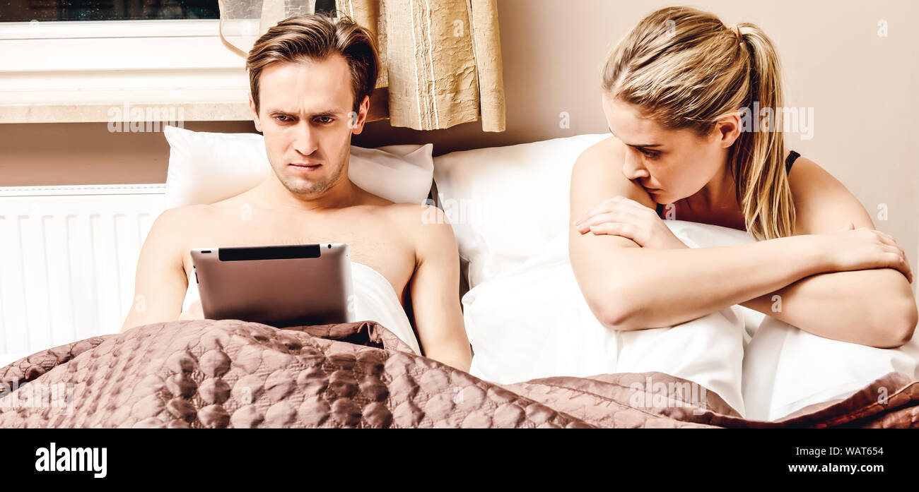 Married Couple In Bed Husband Is Using Tablet And Wife Is