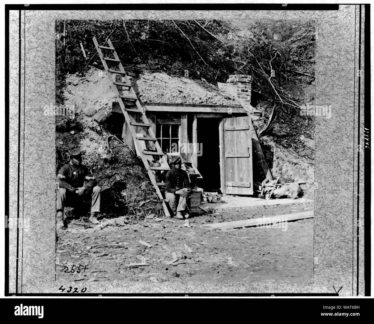 Dutch Gap Canal [...] November 1864, while Canal was being dug Abstract: Two African American soldiers seated in front of small building in bottom of cliff, near Dutch Gap Canal. Stock Photo