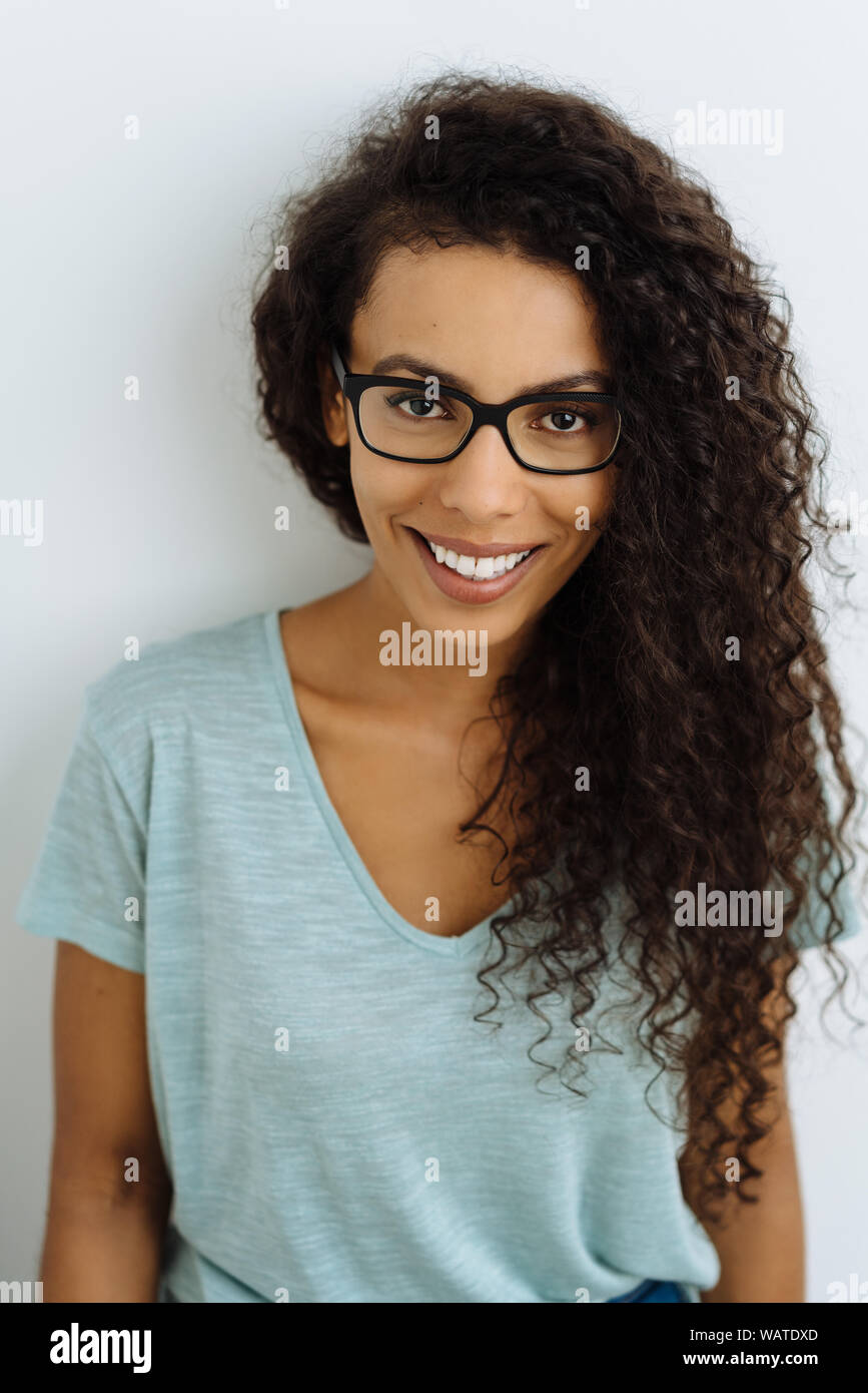 Young woman wearing glasses with a friendly smile and long frizzy black hair  looking at the camera with a happy expression against a white studio back  Stock Photo - Alamy