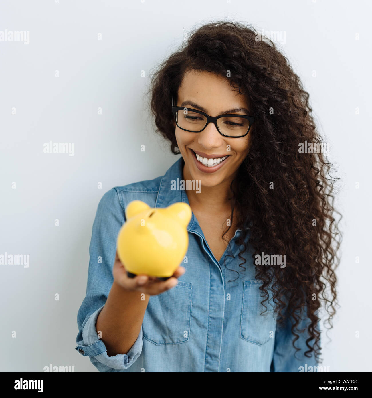 Happy young woman looking at her piggy bank in her hand with a beaming smile of anticipation as she imagines spending her savings against a white stud Stock Photo