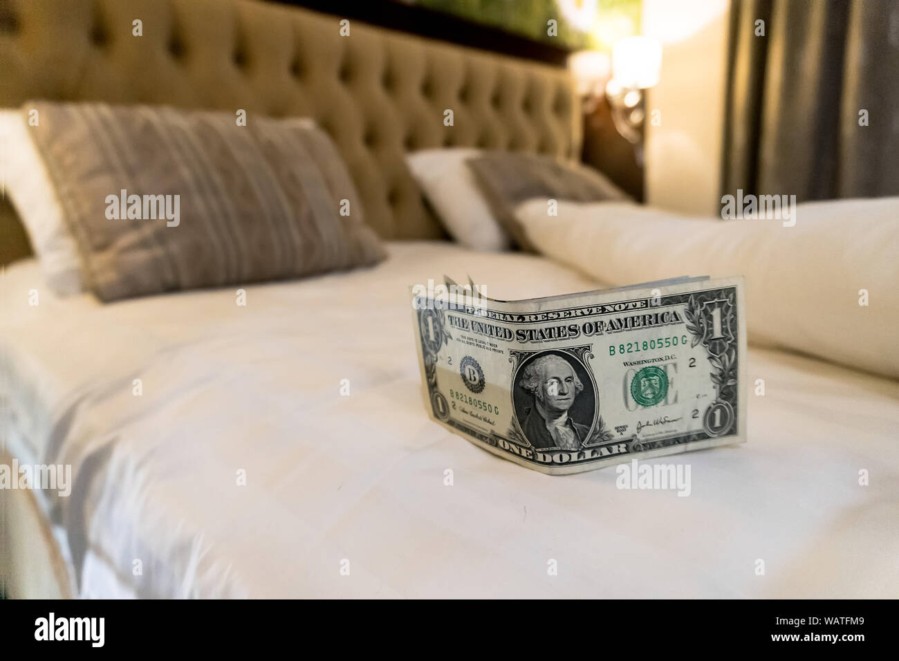 paying us money dollar on white bed in hotel. tips left on the bed for the maid of the hotel room. Tips at the bed for the housekeeper in hotel. Stock Photo