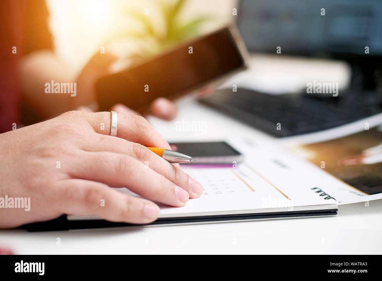 Picture of Man writing on a notebook with a pen and holding mobile in ...