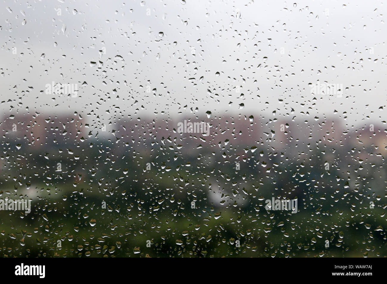 Water drops on the window glass on blurred background of city buildings and cloudy sky. Beautiful raindrops, rainy weather Stock Photo