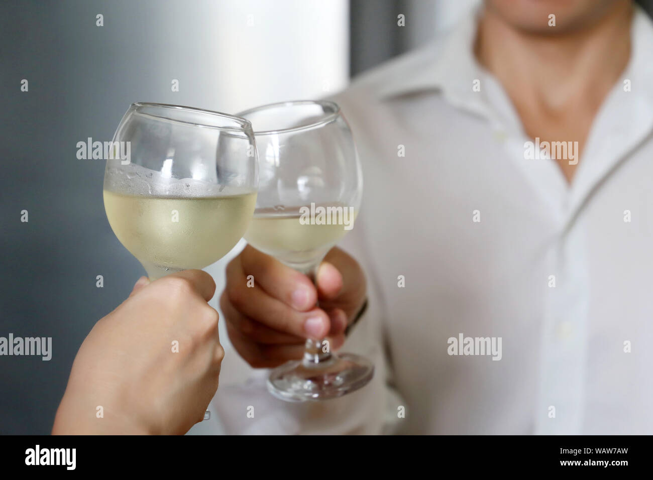 Couple drinking white wine on a romantic date. Woman and man in white shirt clink by misted wine glasses, concept of wedding, celebration, love date Stock Photo