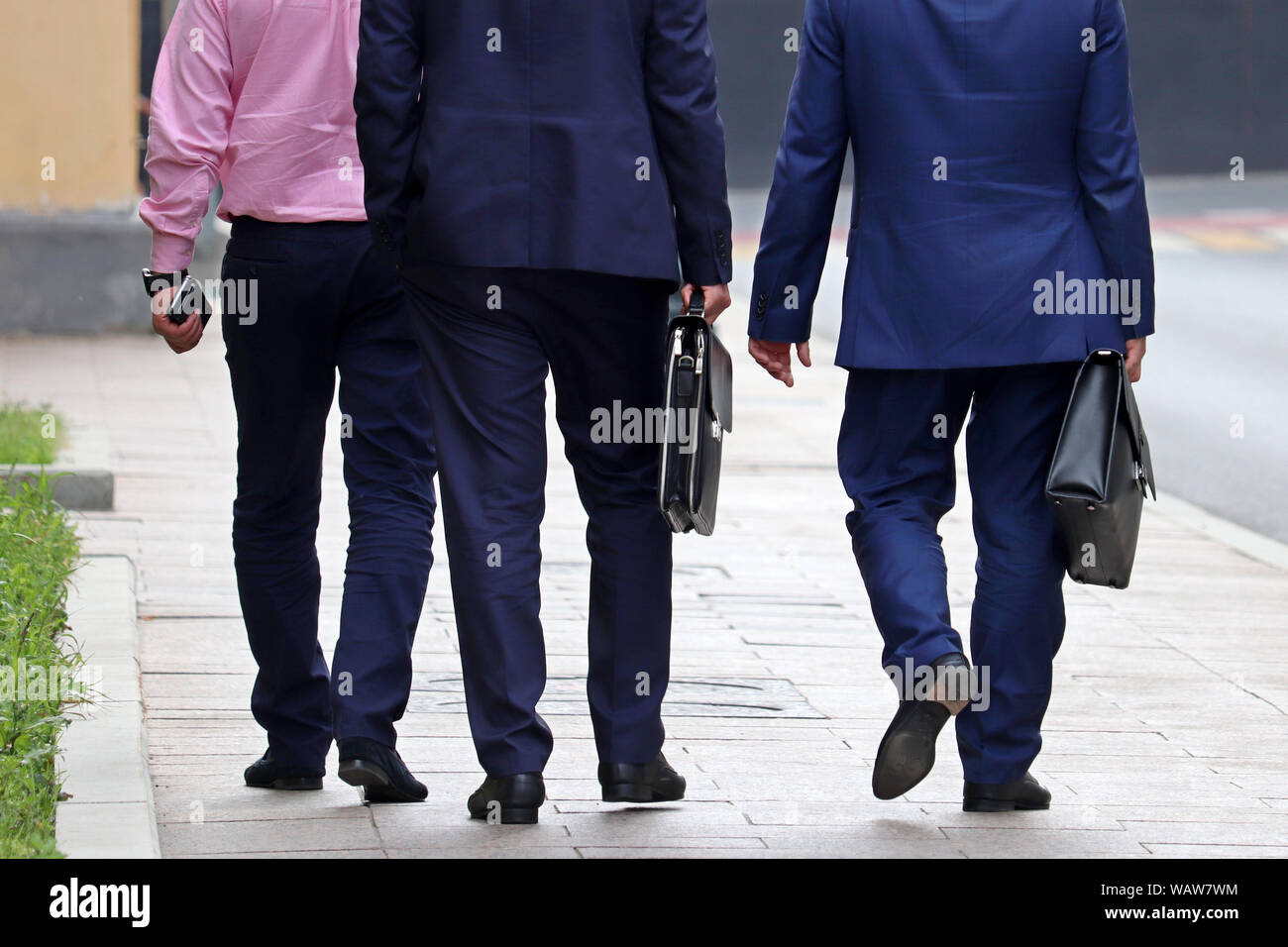 Men in a business suits with briefcases walking on a street, rear view. Concept of stylish successful people, partners, businessmen, official, career Stock Photo