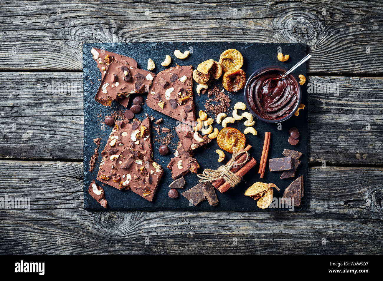 homemade chocolate bar with dried figs and cashew filling on a black stone tray with ingredients, horizontal view from above, flatlay Stock Photo