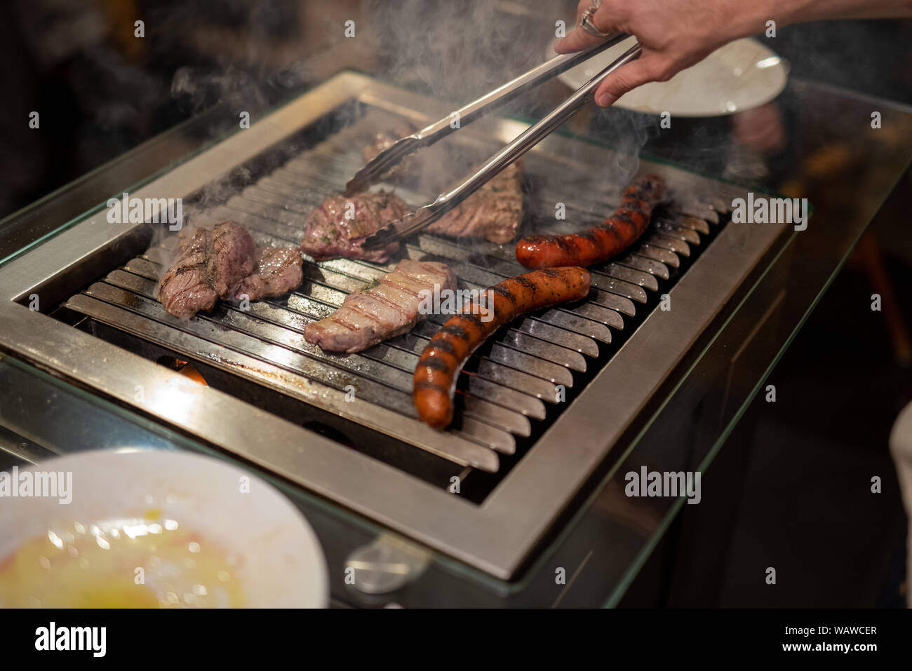 different types of meat, beef steaks and pork sausages, cooked on a grill indoor Stock Photo