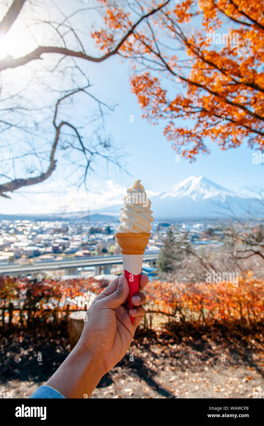 hand holding soft cream ice cream cone with Mount Fuji and colourful autumn maple tree background at Arakurayama Sengen Park - Fujiyoshida Stock Photo
