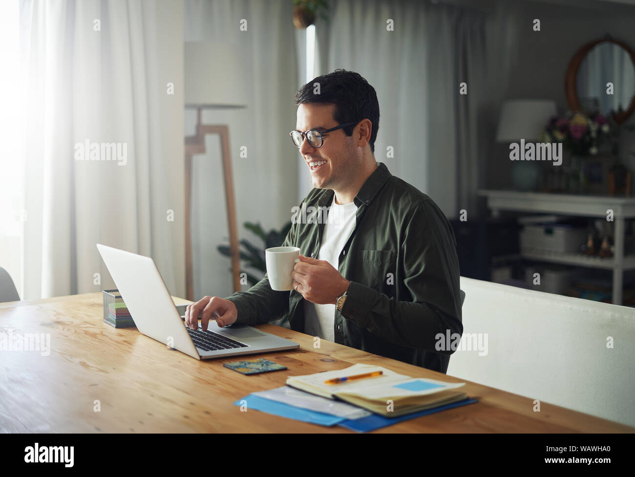 Smiling man enjoying the coffee while using laptop at home Stock Photo