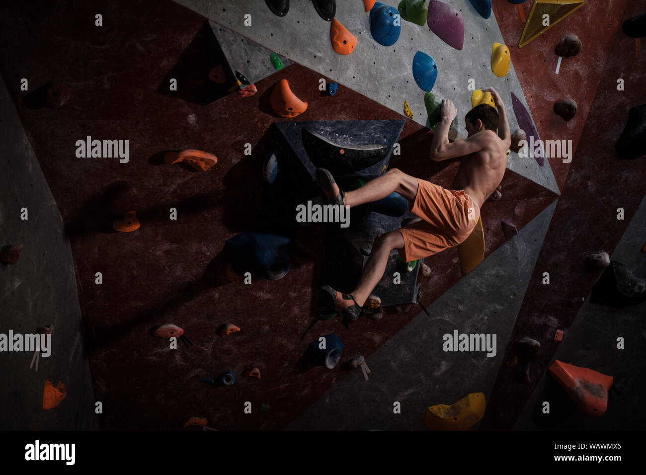 Beautiful young woman in black outfit climbing on practical wall in gym,  bouldering, extreme sport, rock-climbing concept. Stock Photo