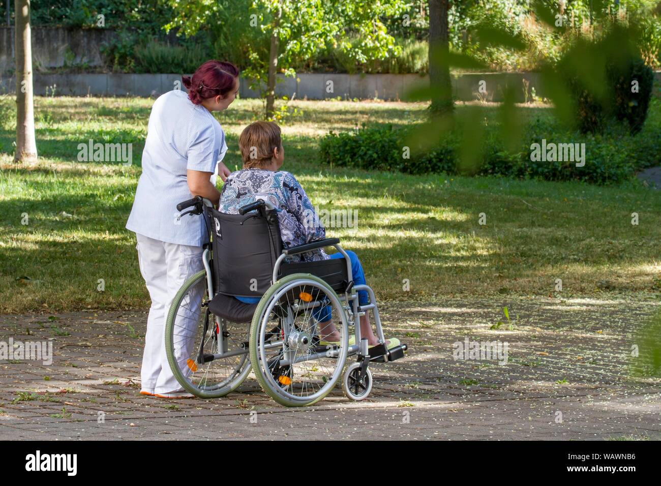 Woman sitting in wheelchair, nurse walking with woman in wheelchair, Germany Stock Photo