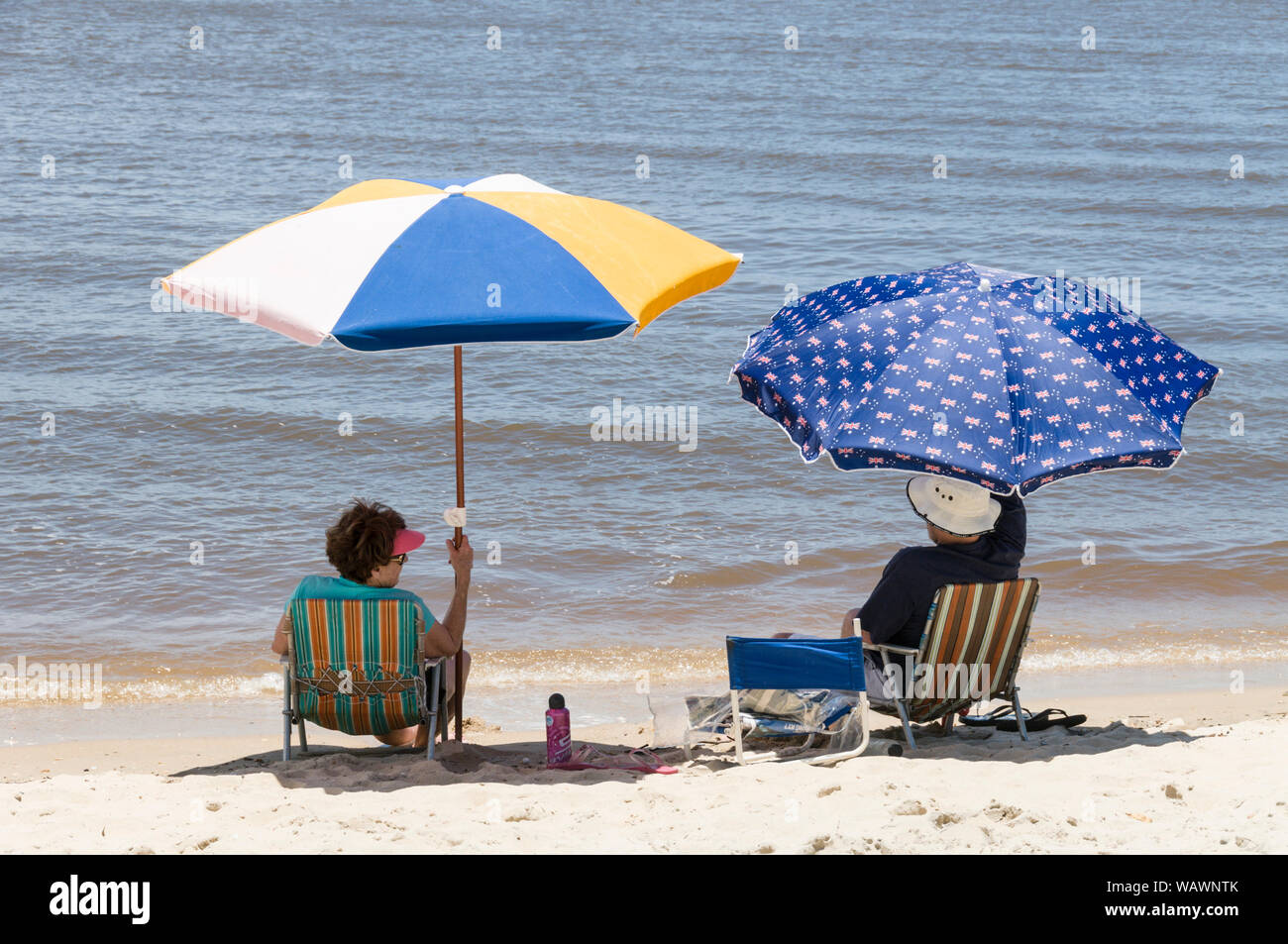 An elderly couple sheltering from hot winter sun on Cotton Tree Caravan park beach at Maroochydore on the Sunshine Coast in Queensland, Australia Stock Photo