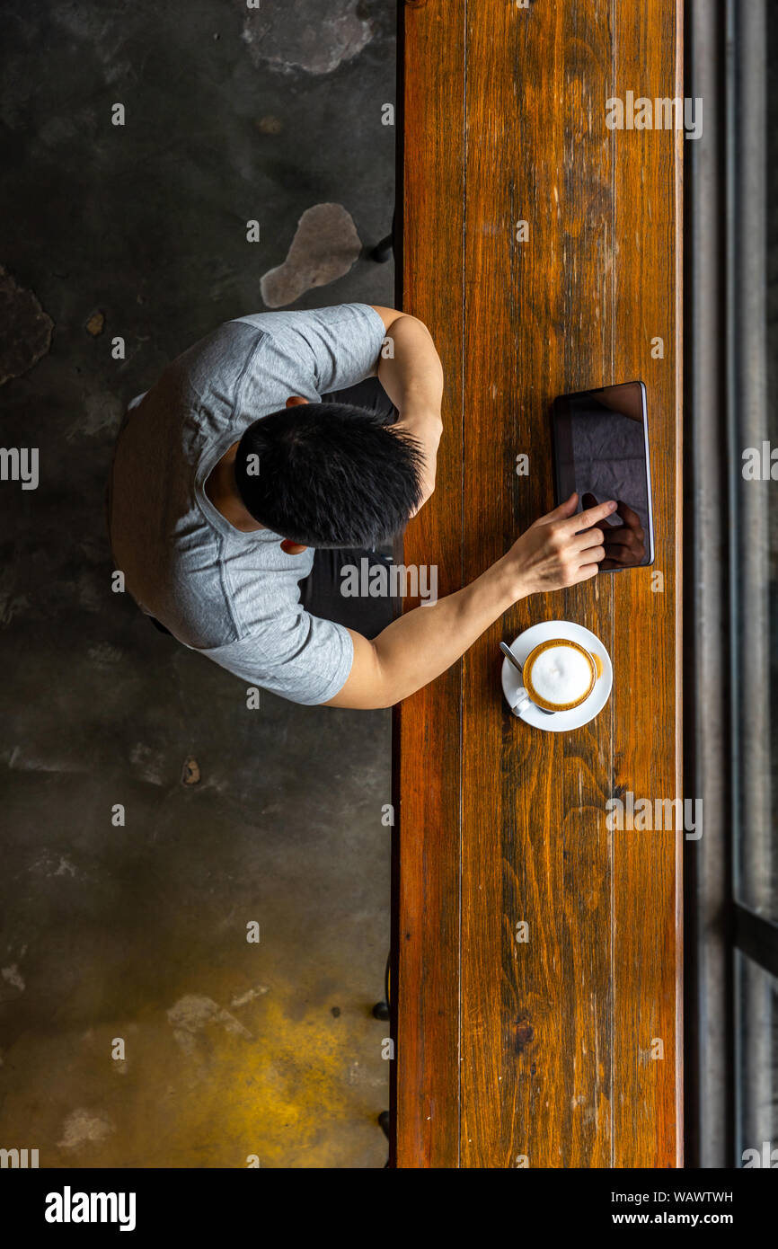 Asian young man using tablet while having hot cappuccino Stock Photo