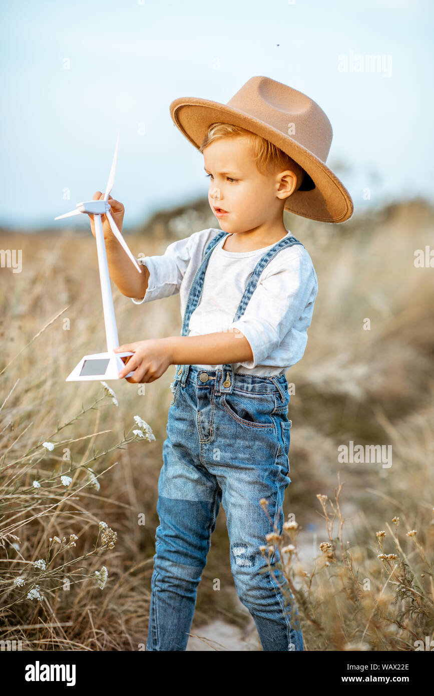 Curious young boy playing with toy wind turbine in the field, studying how green energy works from a young age Stock Photo