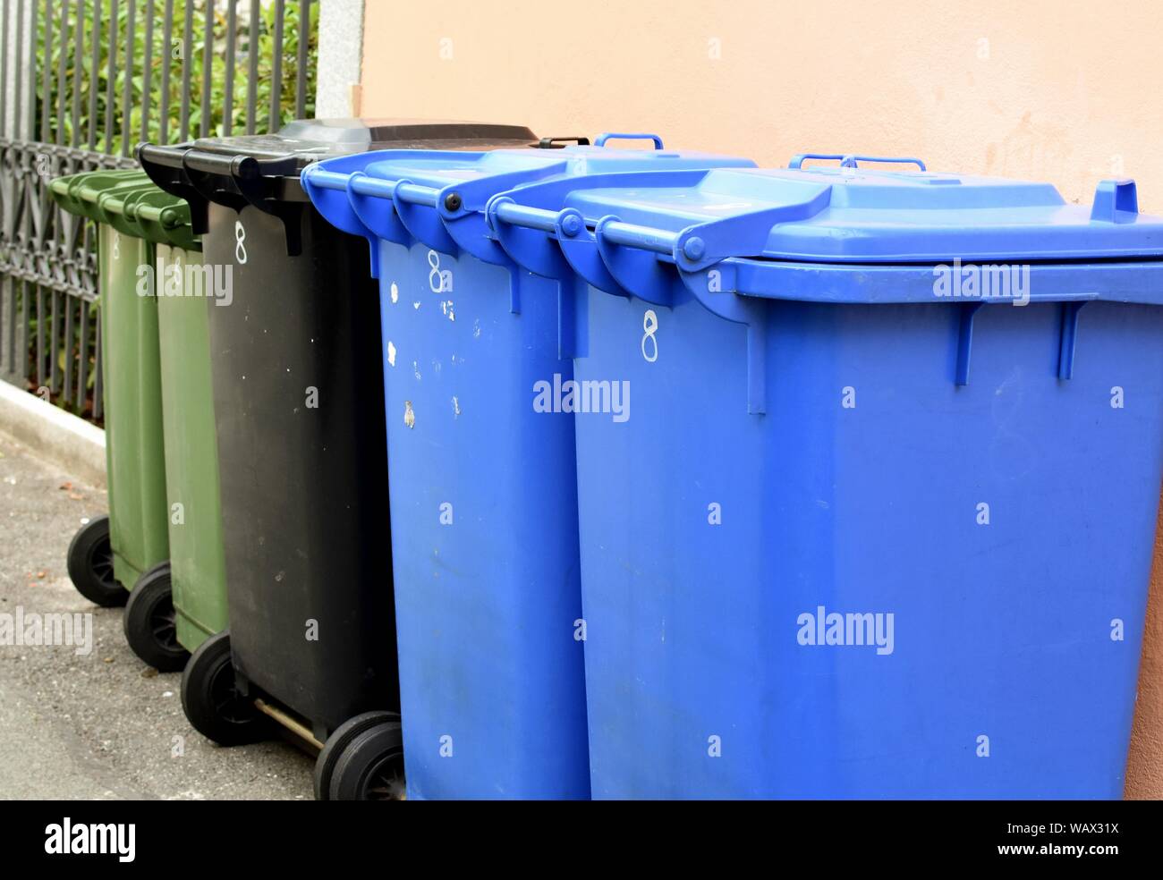 Plastic garbage containers along the wall on the street. Stock Photo