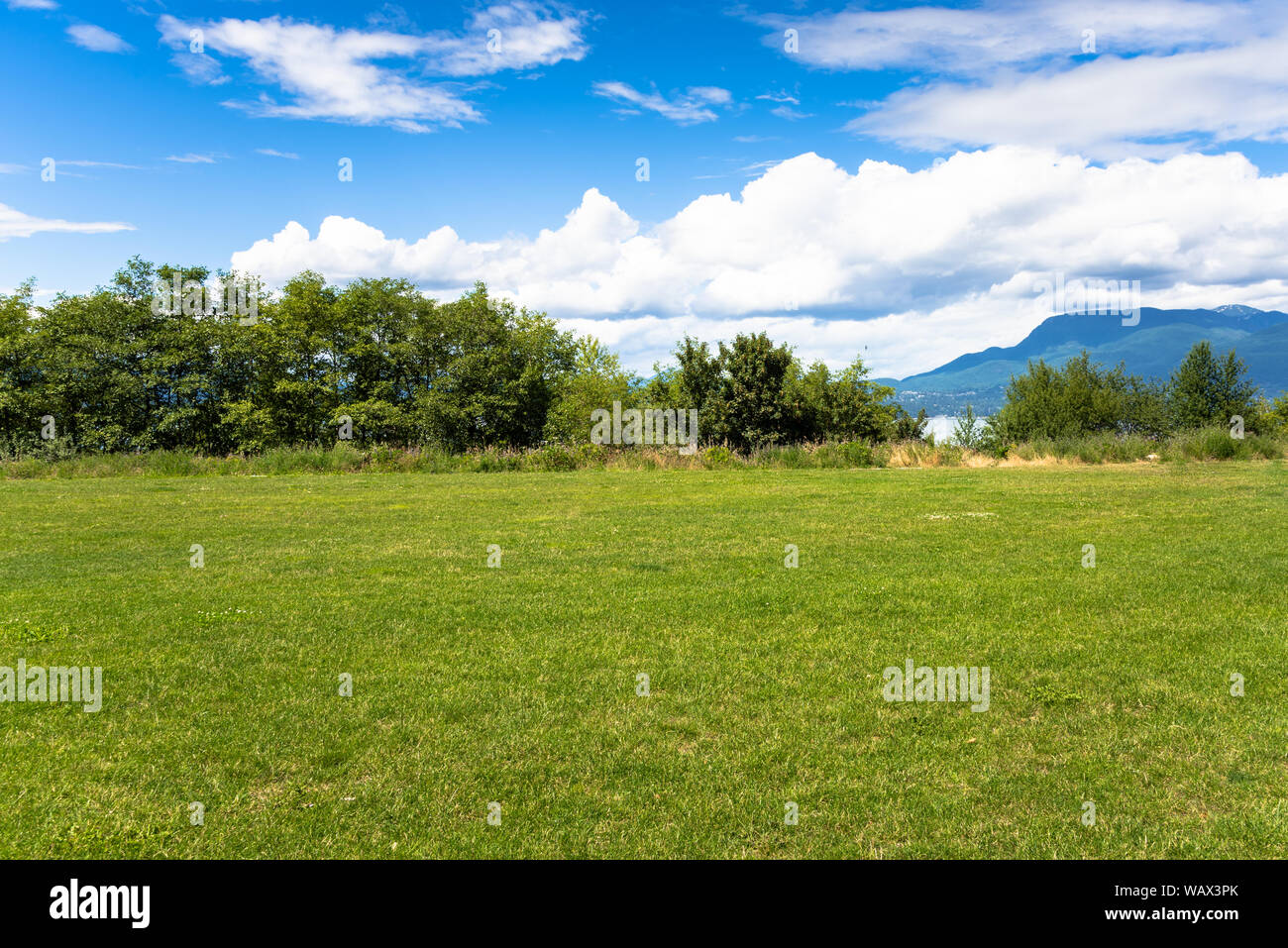 Deserted meadow in a coast park with sea and mountains in background on a sunny summer day Stock Photo