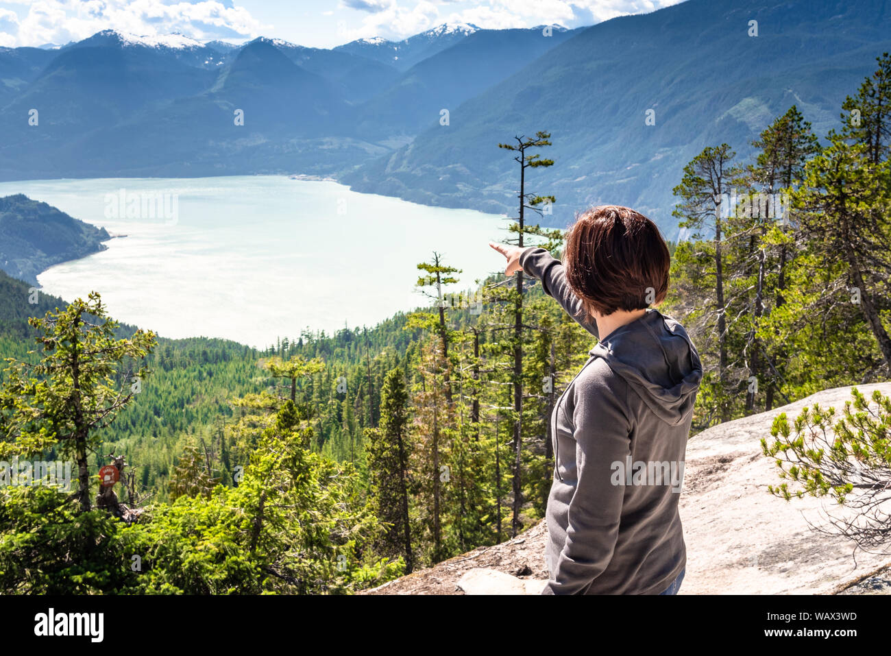 Woman hiker pointing at the beautiful scenery while staind on the top of a mountain on a sunny summer day Stock Photo