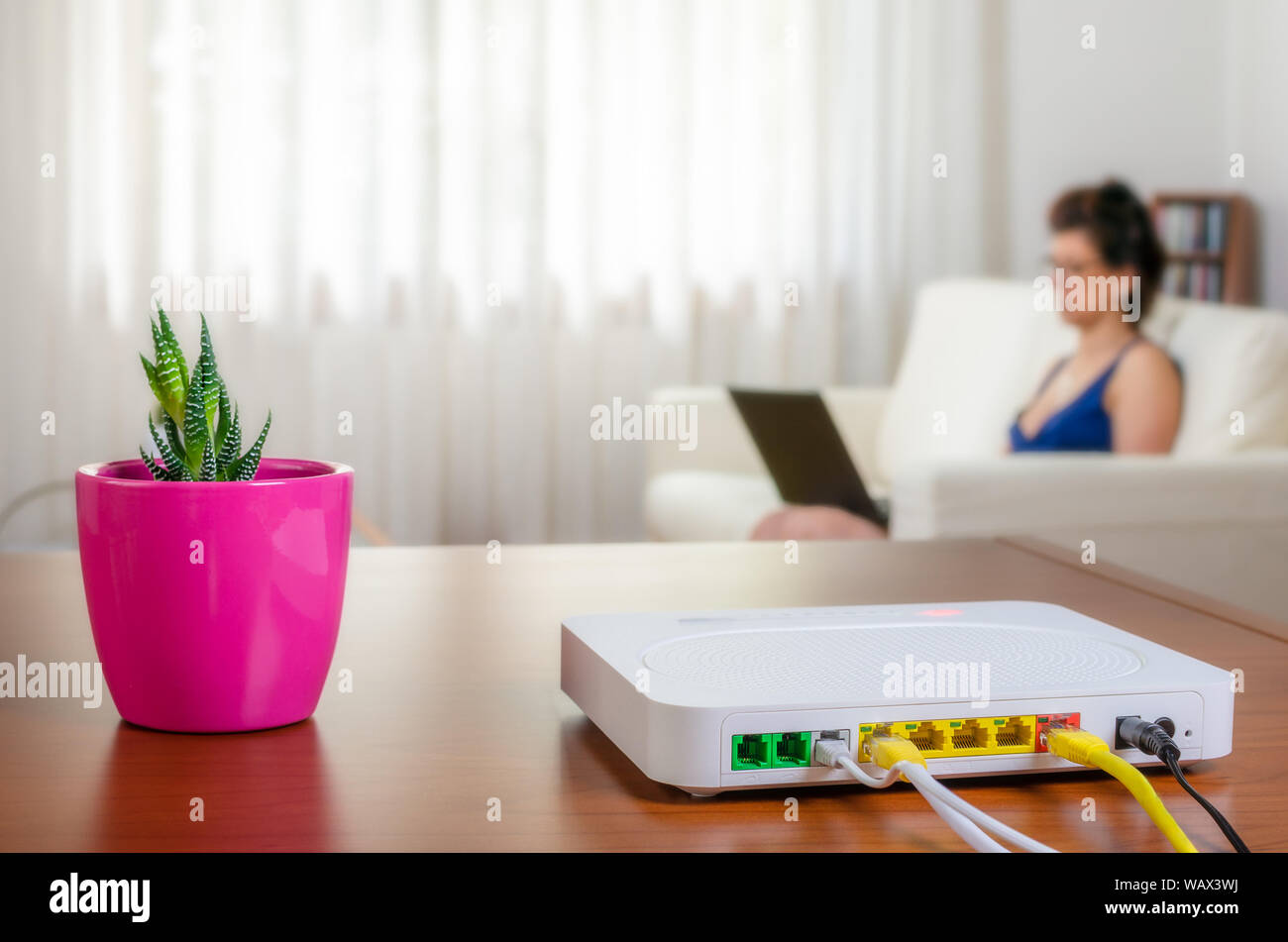 Modem router on a table in a living room with a woman using a laptop while  sitting on a sofa in background Stock Photo - Alamy
