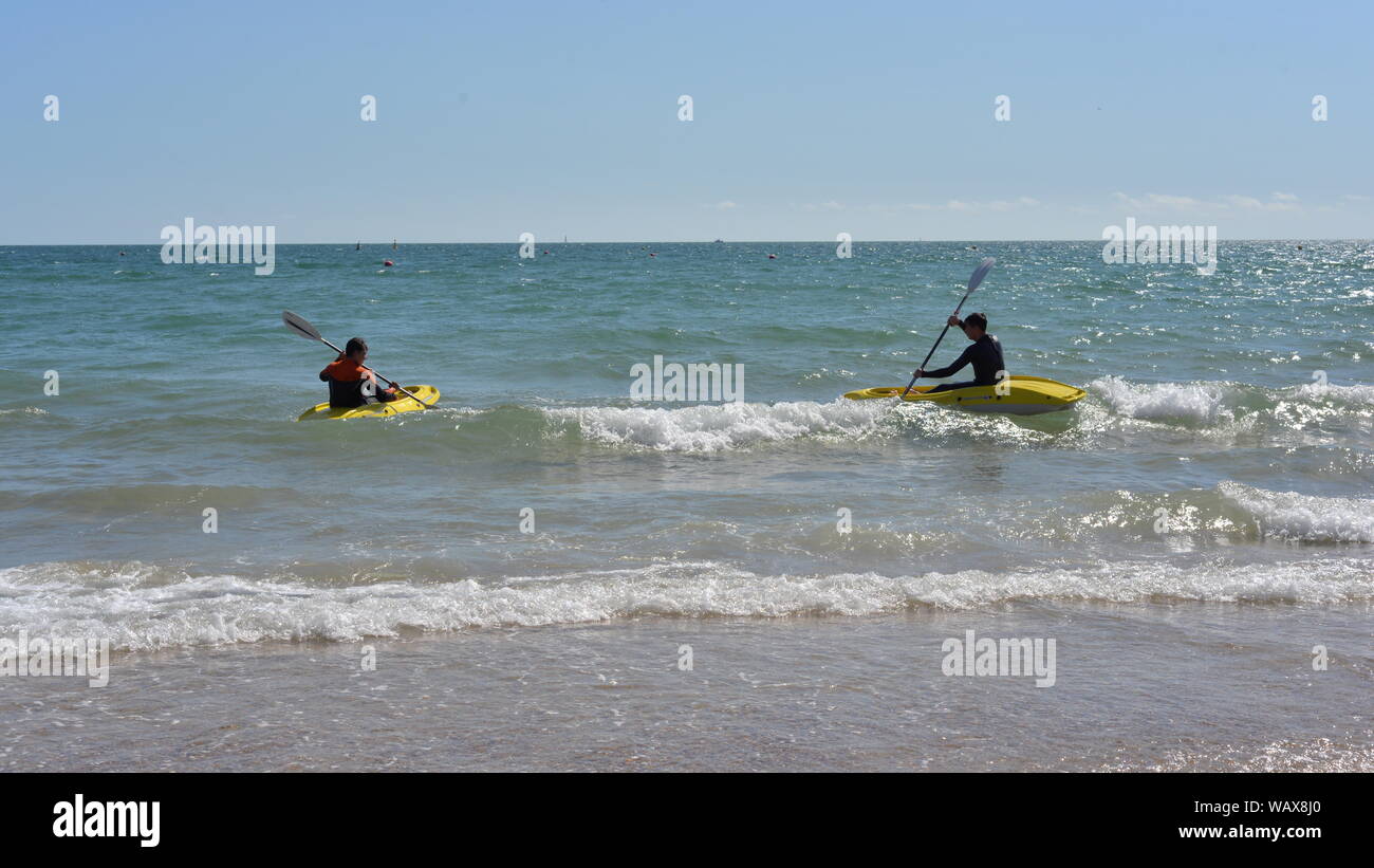 Boscombe, Bournemouth, Dorset, England, UK. 22nd August, 2019. Weather: Warm and sunny afternoon on the south coast beach with temperatures rising into the bank holiday weekend accompanied by a good dose of late summer hot sunshine. Two kayakers riding over waves and out to sea. Stock Photo