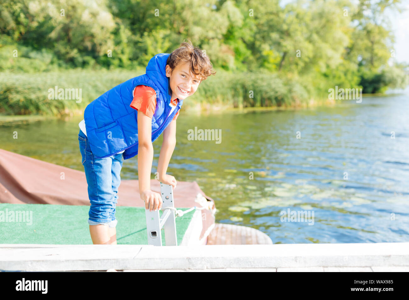 Beaming dark-haired boy smiling while standing near lake Stock Photo
