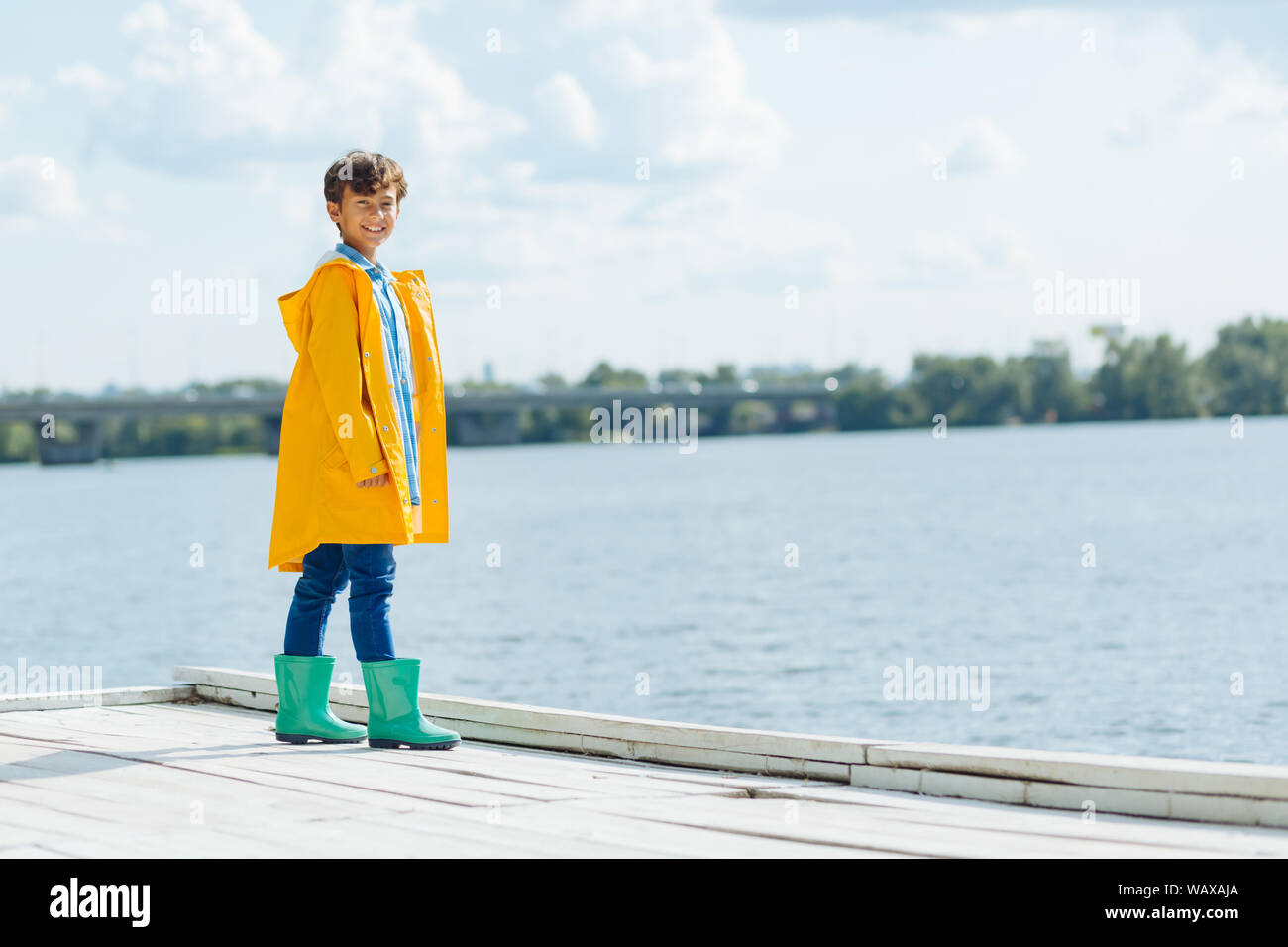 Boy wearing raincoat smiling while enjoying river view Stock Photo