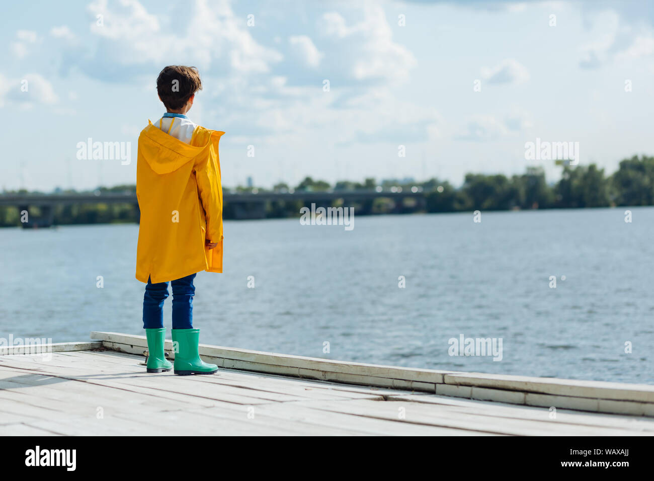 Dark-haired boy wearing yellow raincoat and wellingtons Stock Photo