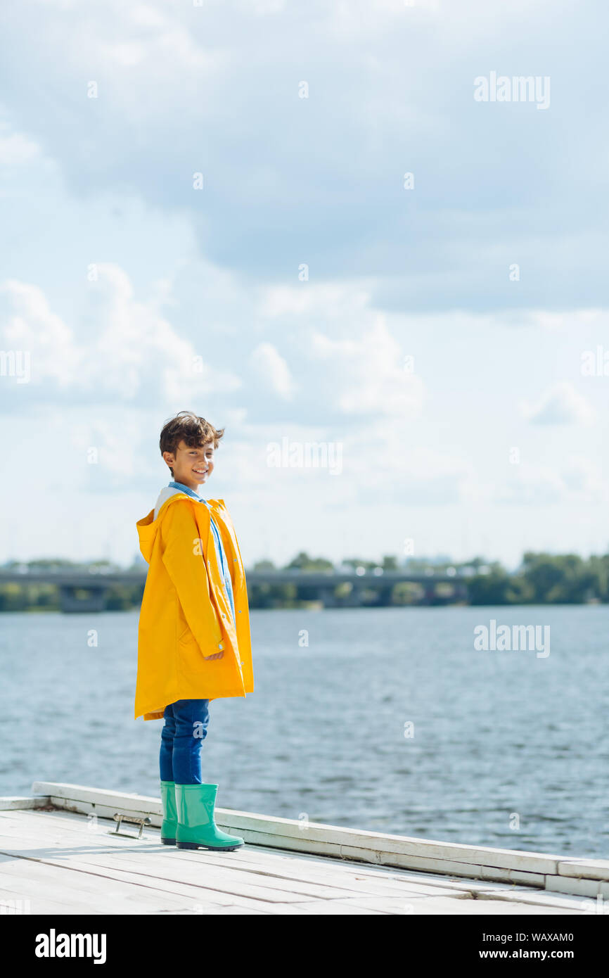Handsome boy wearing bright rain boots standing near river Stock Photo