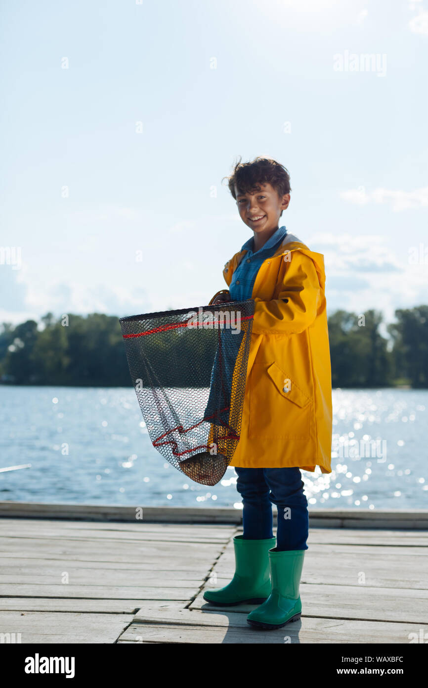 Cheerful boy wearing raincoat holding fishing net Stock Photo - Alamy