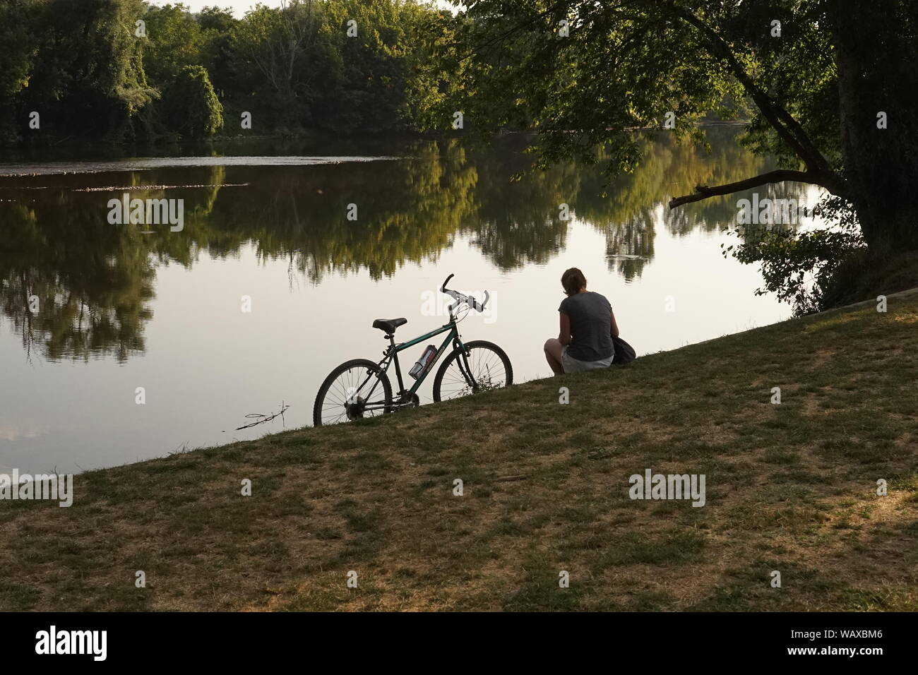 A lady with her bike sitting beside the Dordogne river in France taking in her surroundings Stock Photo