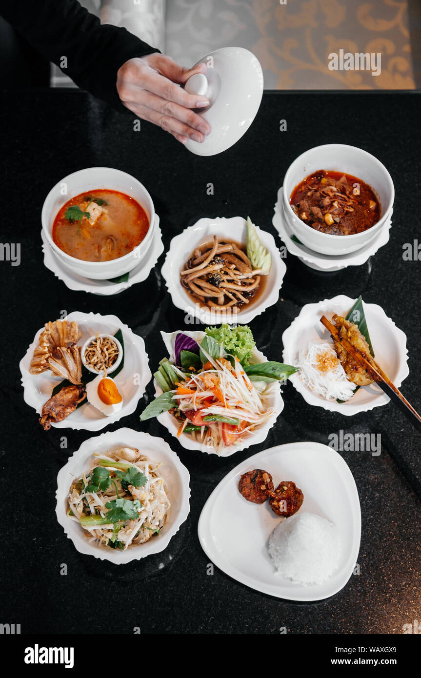 Assorted Traditional Thai food, red Massaman curry, Tom Yum spicy soup, Papaya salad, Grilled chicken and local dishes on black table top view shot Stock Photo