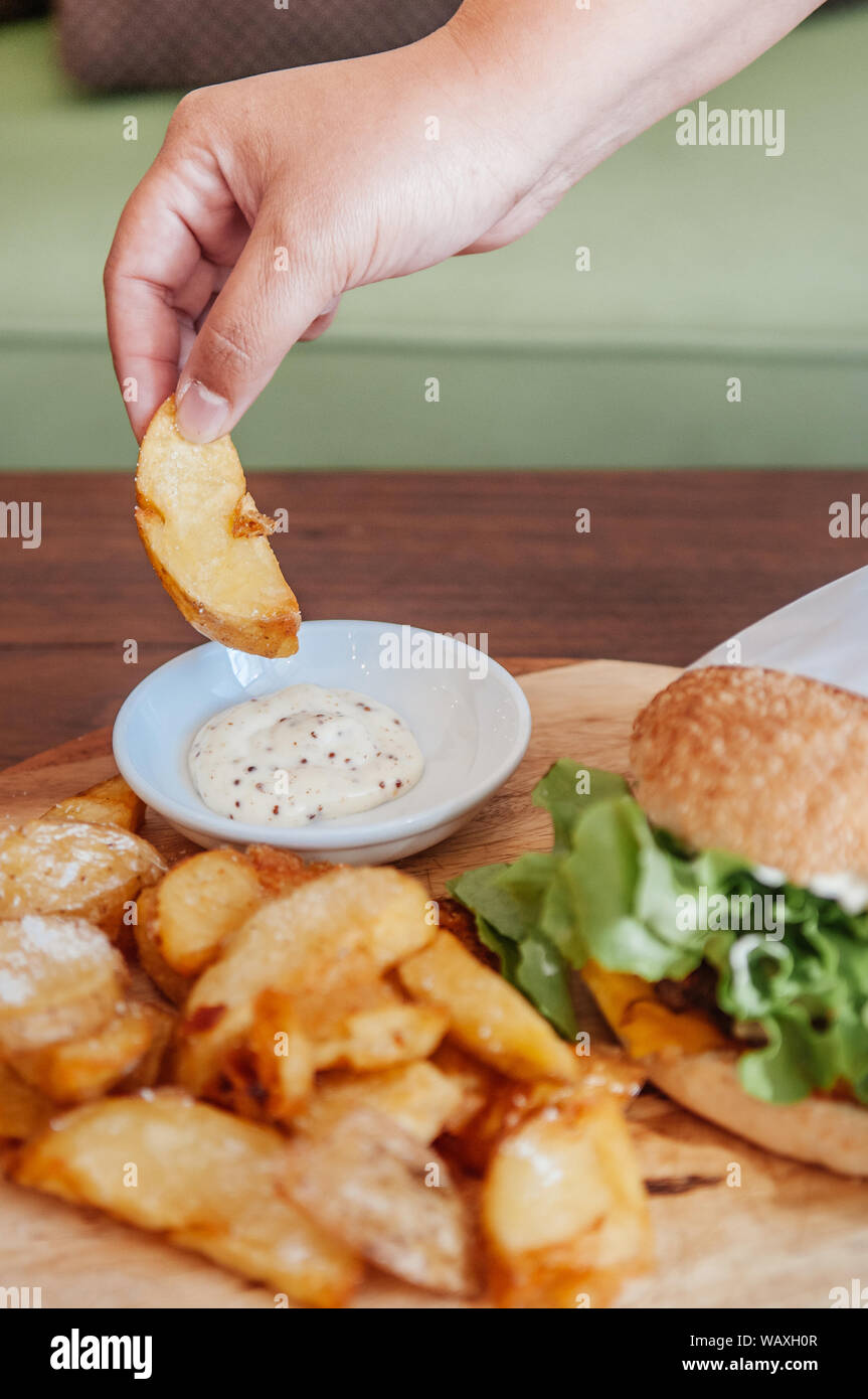 Beef cheeseburger and hand picking fried potato chunks with ranch ...