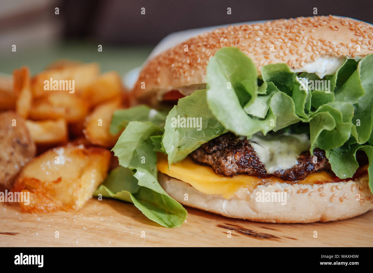 Beef cheeseburger, fried potato chunks with ranch dipping sauce on wood ...