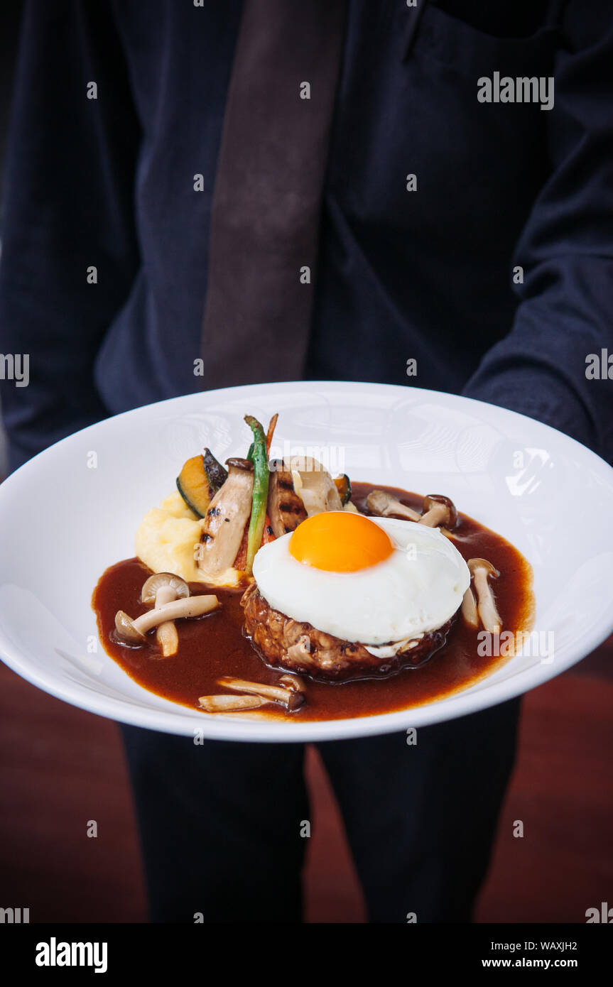 Waiter serving Japanese hamburger steak with sunny side up egg