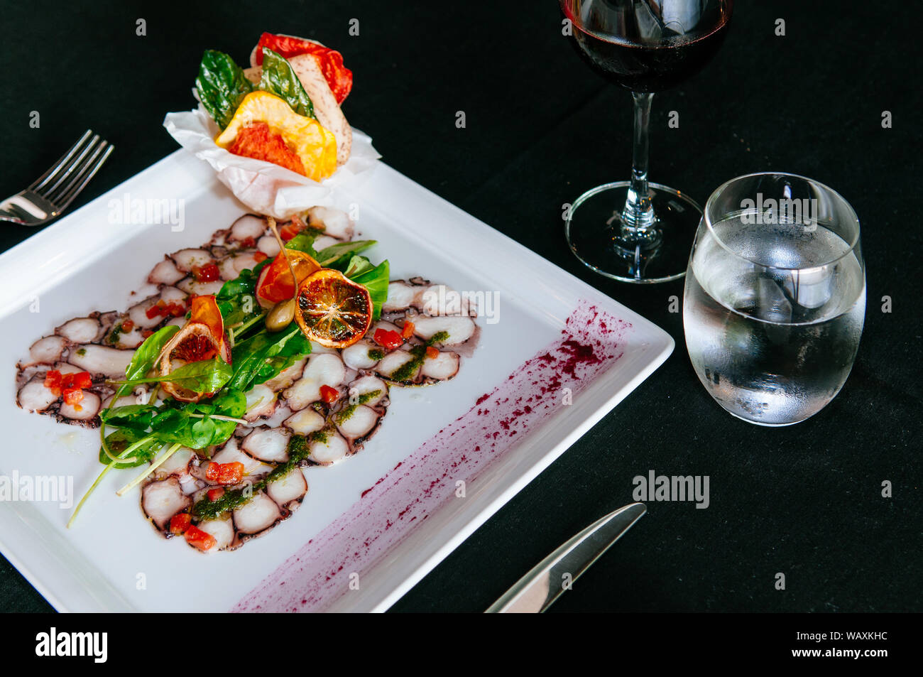 Fresh octopus carpacio with citrus spinach salad pesto balsamic dressing, fine dinning table setting Stock Photo